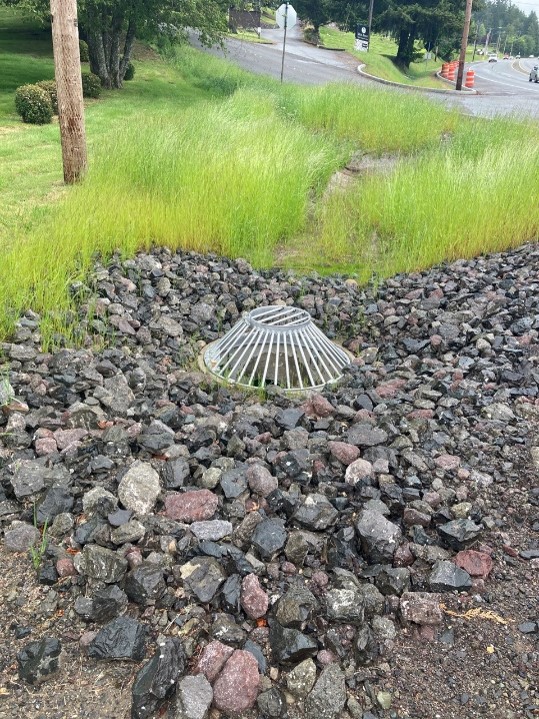 A domed stormwater drain among gravel and grass 